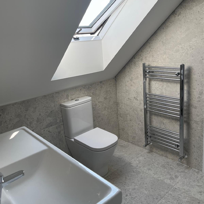 A newly finished bathroom with toilet, sink and heated towel rail.